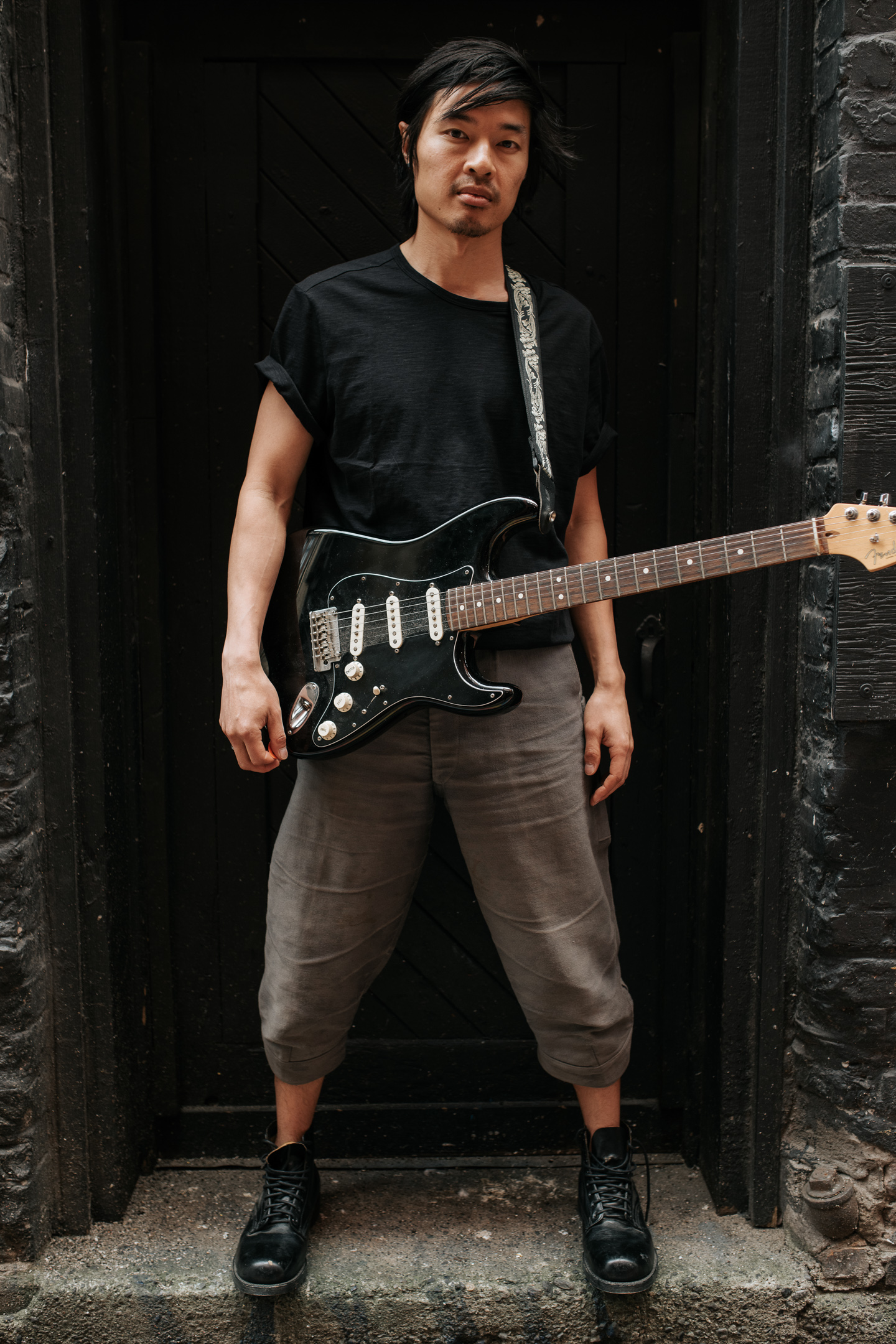 Portrait of Daniel Lew, standing in a wide stance with a black electric guitar.