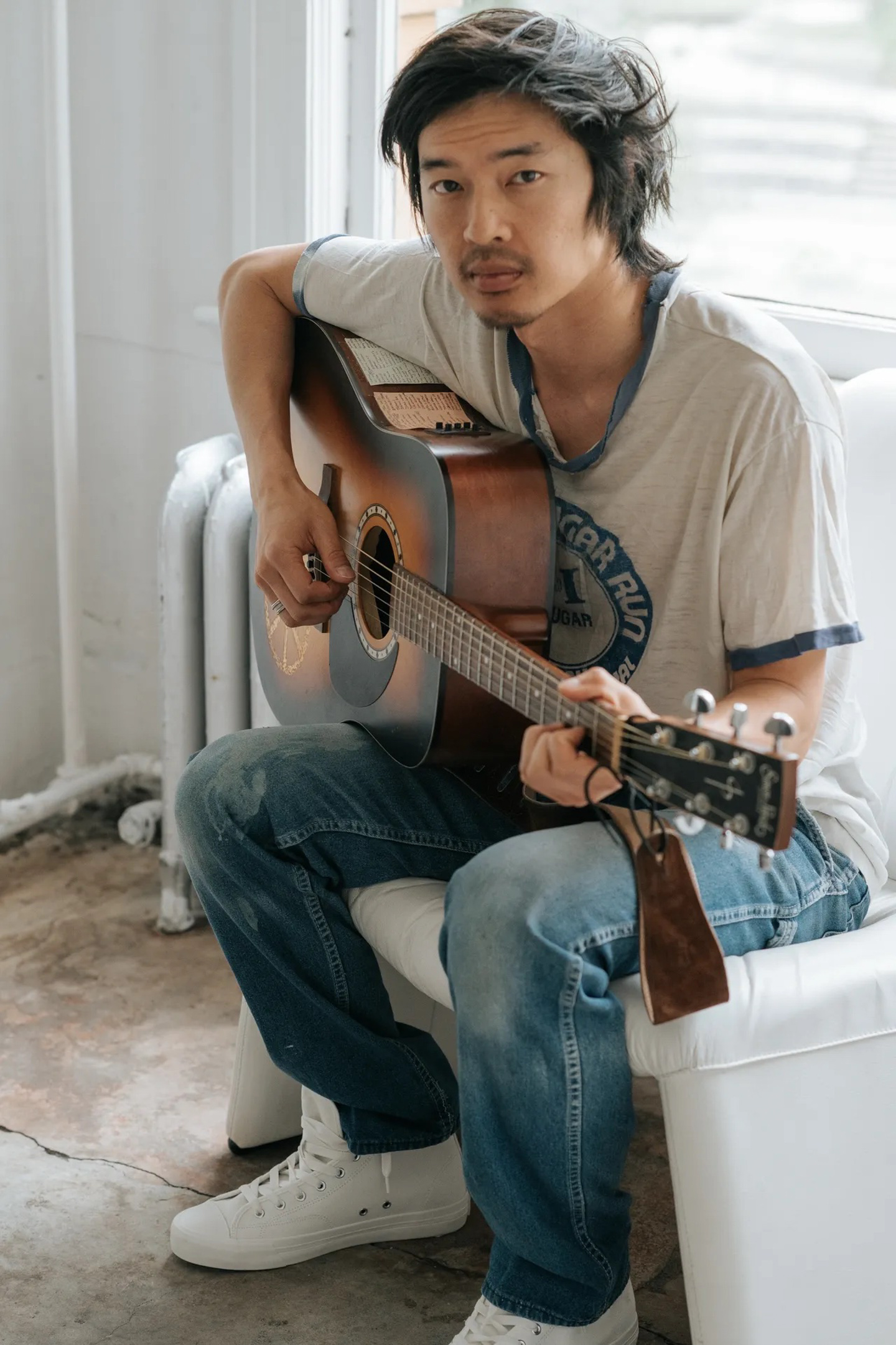 Portrait of Daniel Lew, sitting in a chair holding a brown guitar.